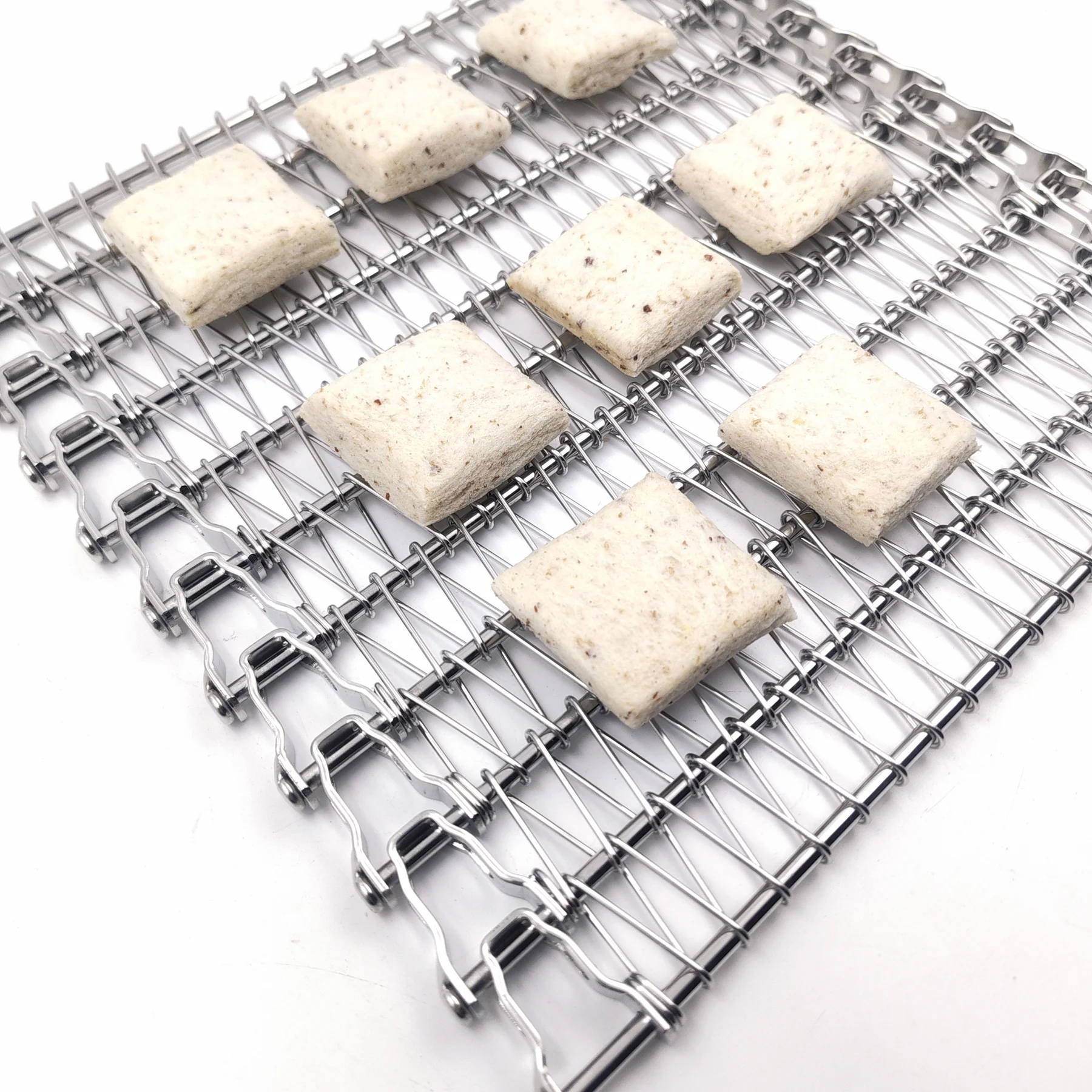 Square prepared food portions arranged on a chain-edged open metal conveyor belt.