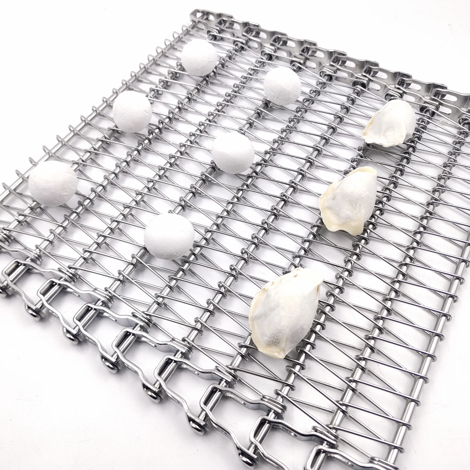 White round and dumpling-shaped food portions arranged on an open metal conveyor belt.