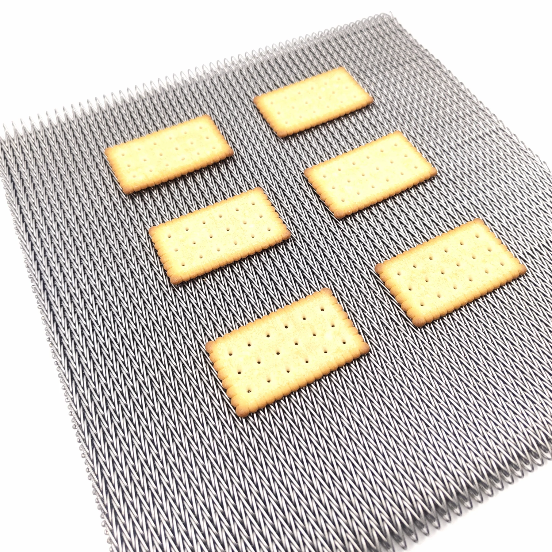 Rectangular biscuits arranged on a fine woven metal conveyor belt against a white background.