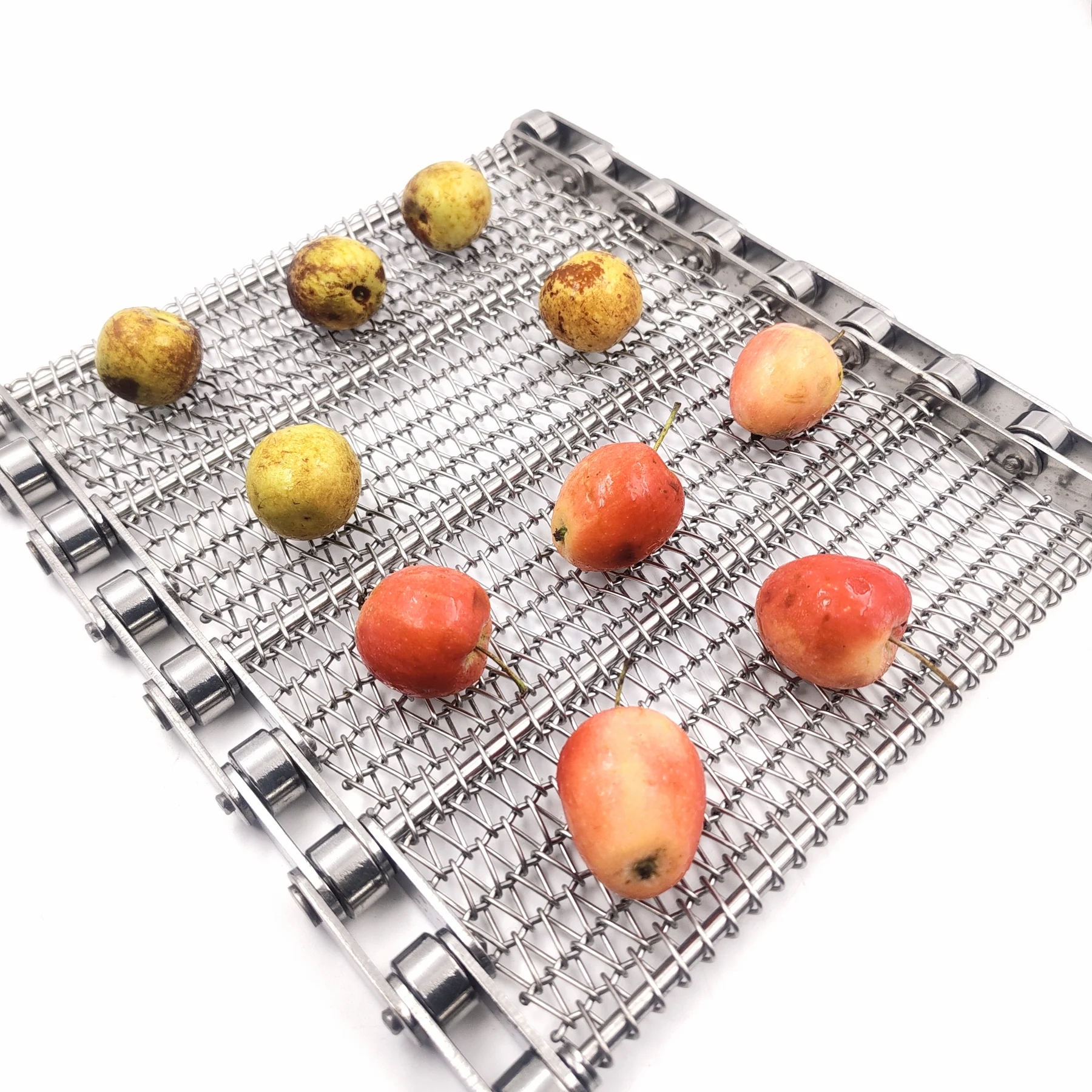 Mixed red and yellow whole fruit displayed on a chain-edged metal mesh belt.