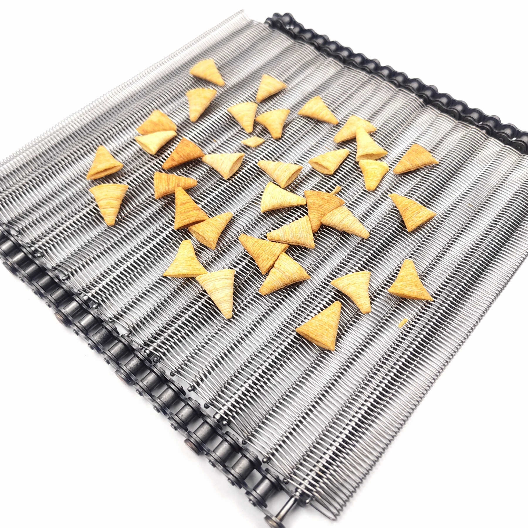 Golden cone-shaped snack pieces arranged on a fine metal conveyor belt.