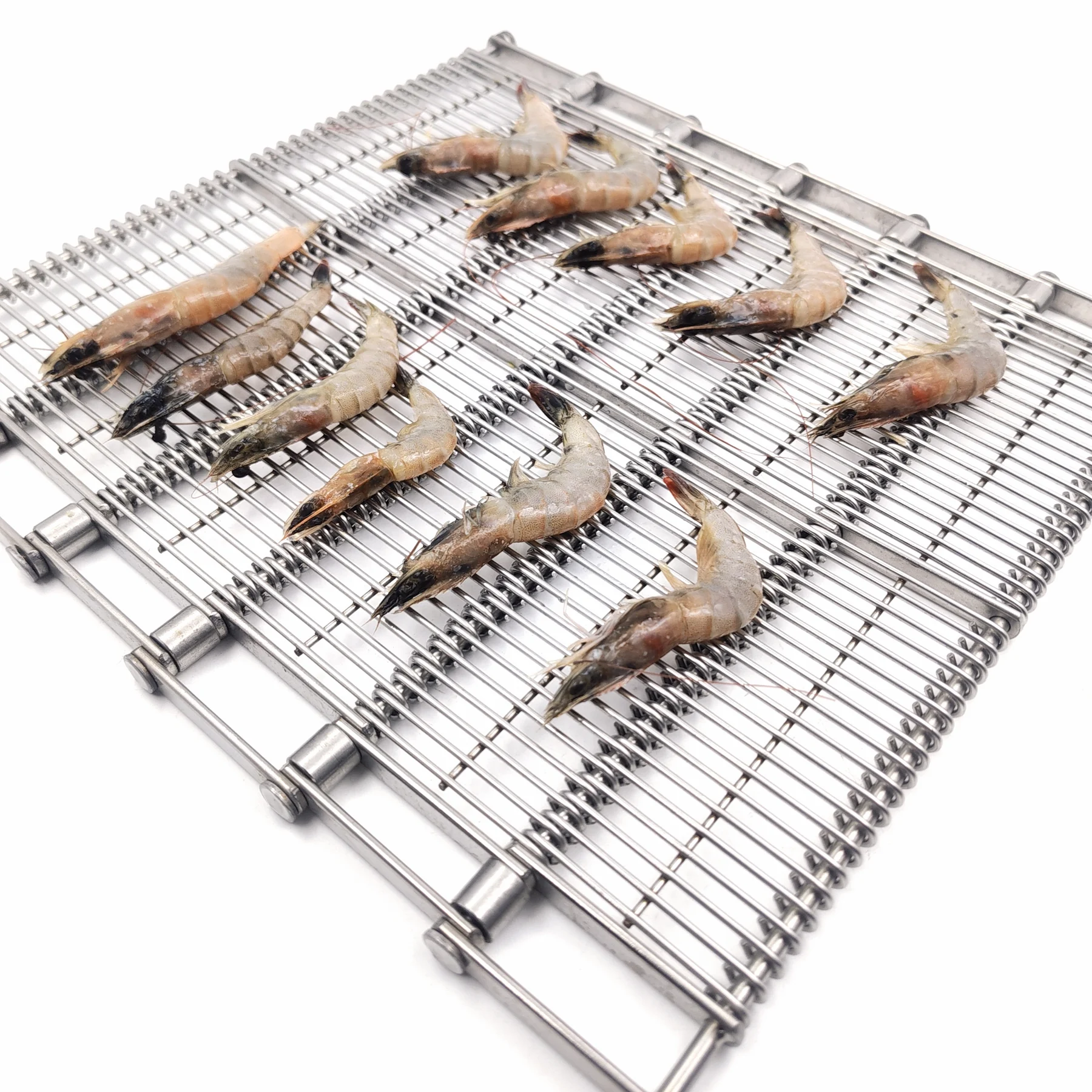 Whole shrimp arranged on a linked open-wire metal conveyor belt.